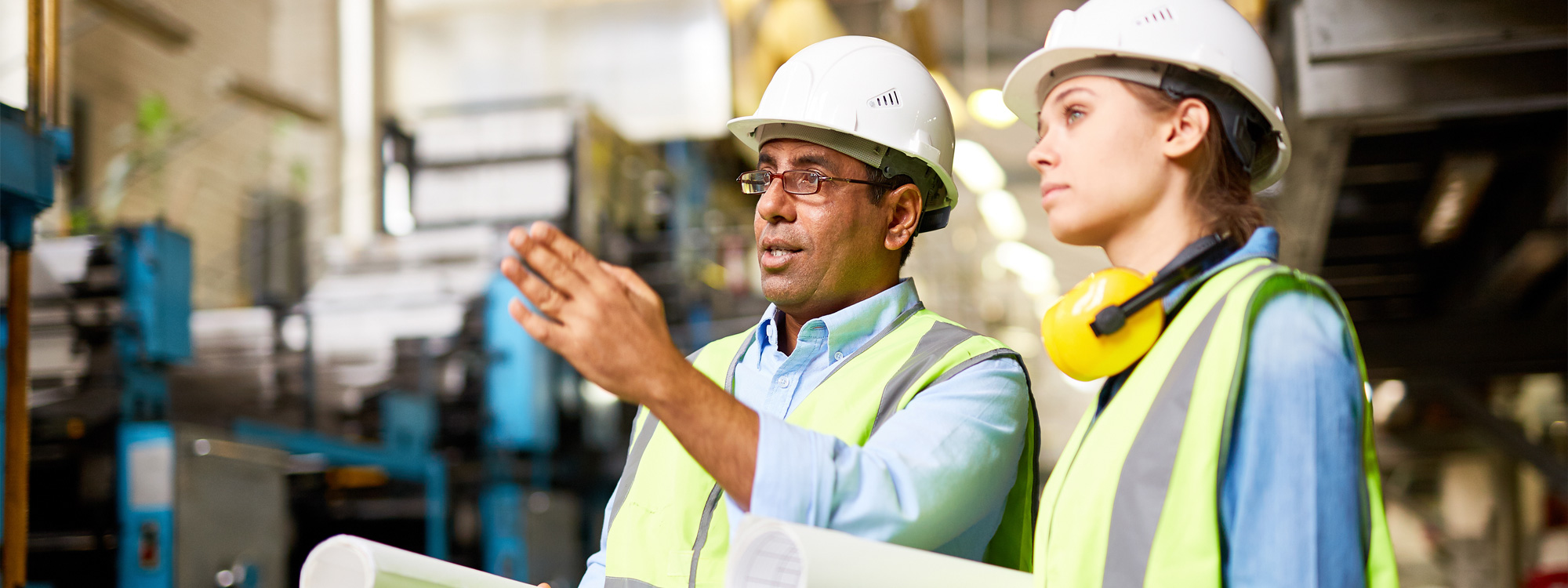 man in hard hat talking to woman in hard hat and point elsewhere